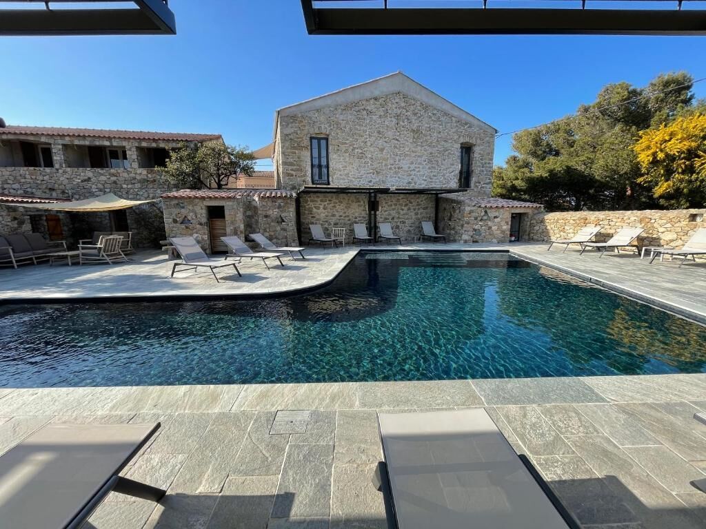 A stone building with a swimming pool and lounge chairs.