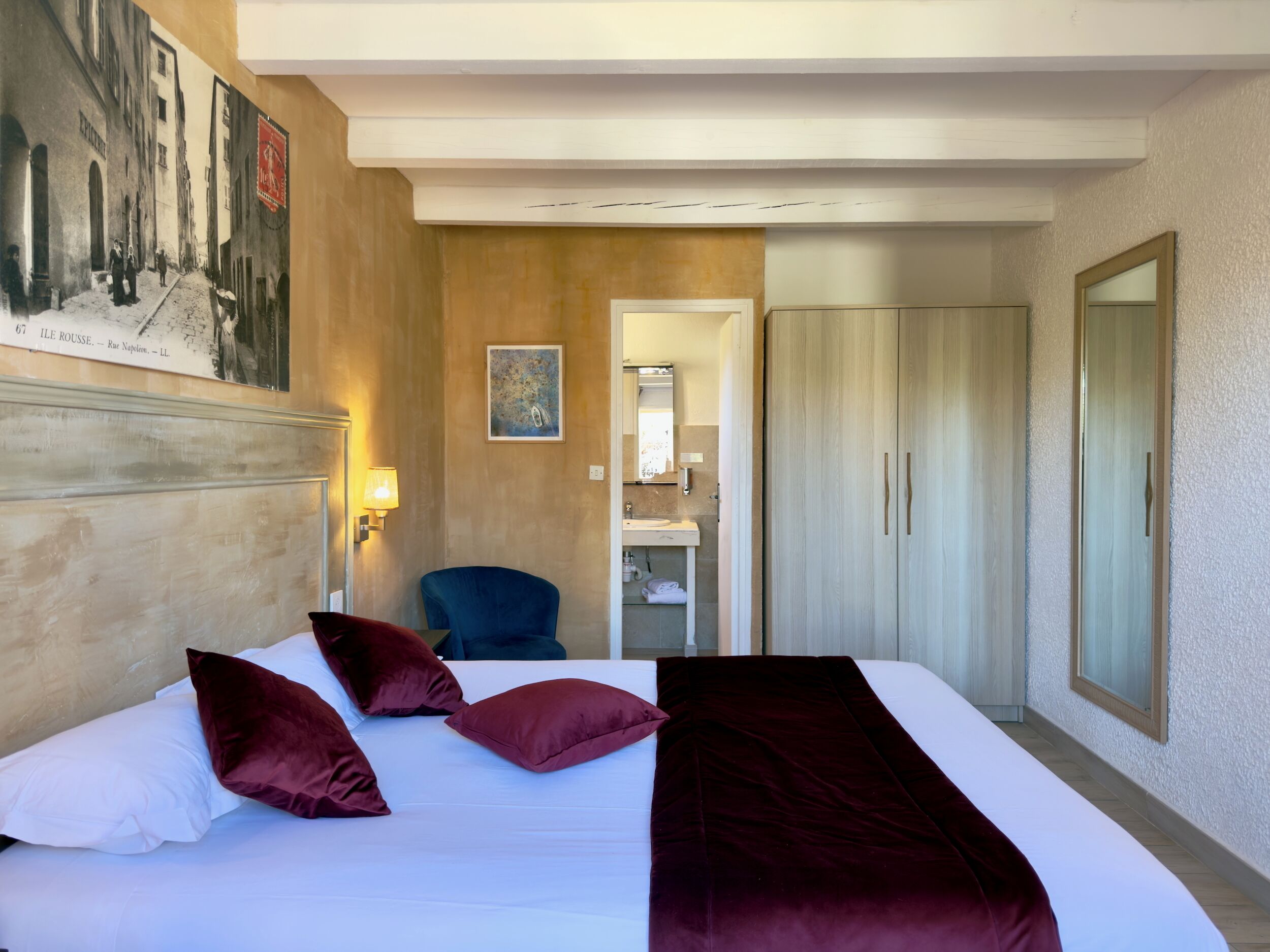 A hotel room with a bed, a chair, a wardrobe, and a bathroom visible through an open door.