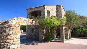 A stone building with a tiled roof, an arched entrance, and a small garden area with trees.