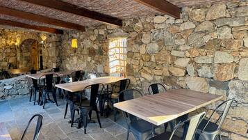 Un área de comedor al aire libre con muros de piedra y mesas y sillas de madera.