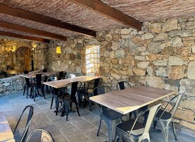 Un área de comedor al aire libre con muros de piedra y mesas y sillas de madera.