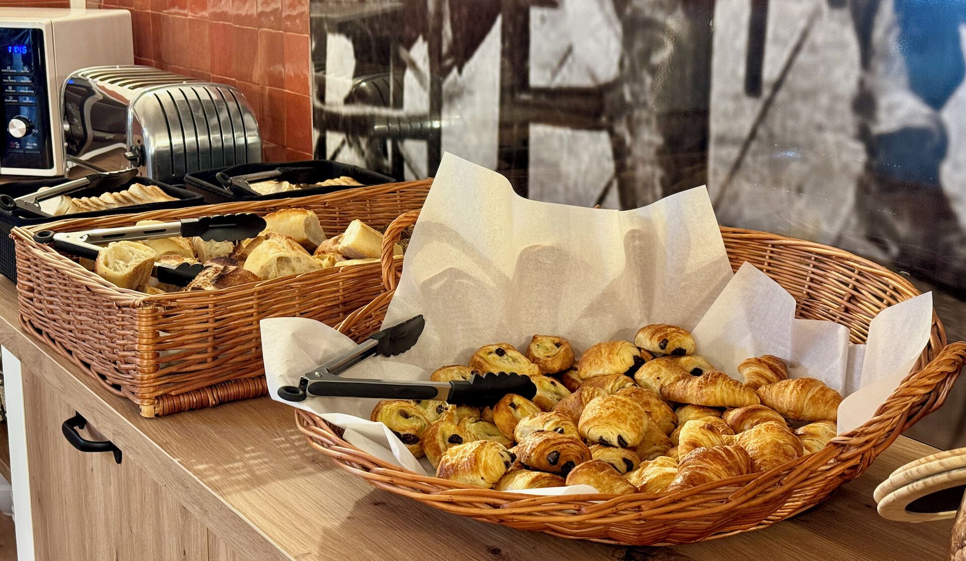 Un buffet proposant une variété de viennoiseries et de pains, notamment des croissants et des baguettes, sur un comptoir en bois.
