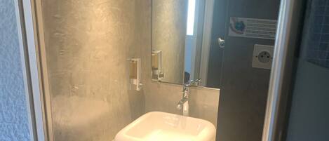 Une petite salle de bain avec un lavabo blanc, un miroir et une étagère à serviettes.