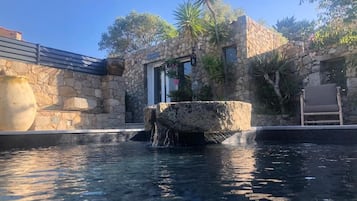 A stone building with a pool, a stone fountain, and a chair.