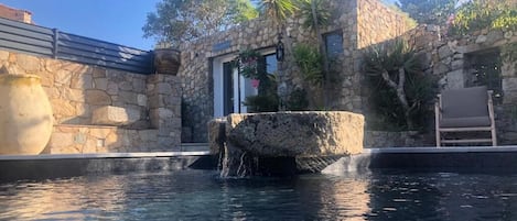 A stone building with a pool, a stone fountain, and a chair.