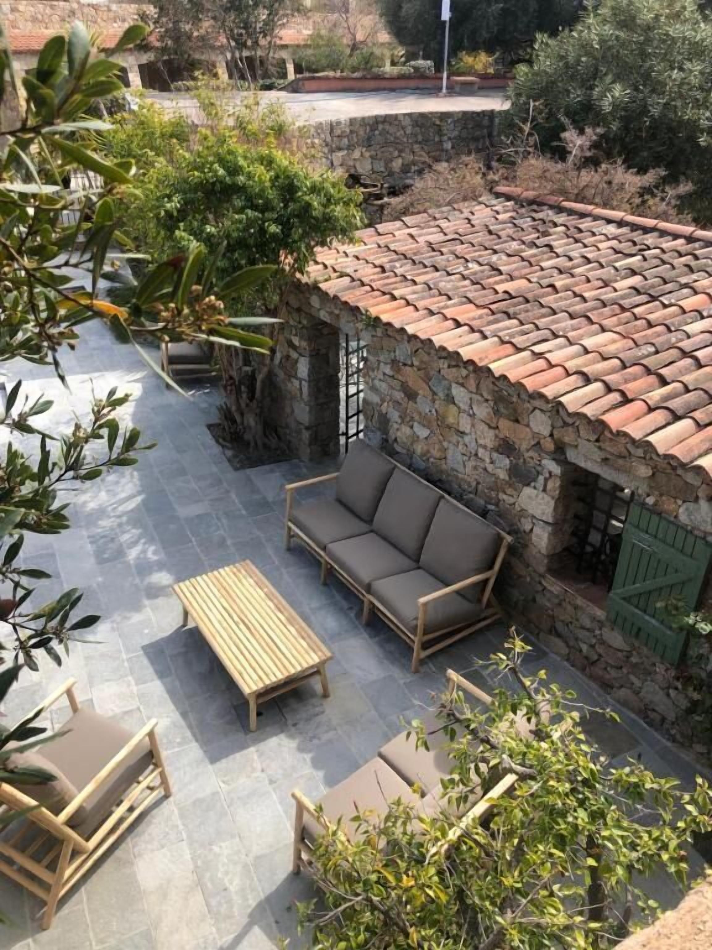 Un bâtiment en pierre avec un toit en tuiles, un banc en bois et un canapé rembourré dans un espace patio extérieur.