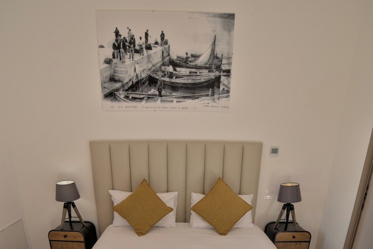 Un lit avec une tête de lit, deux oreillers, une table de chevet avec une lampe et un tableau accroché au mur.