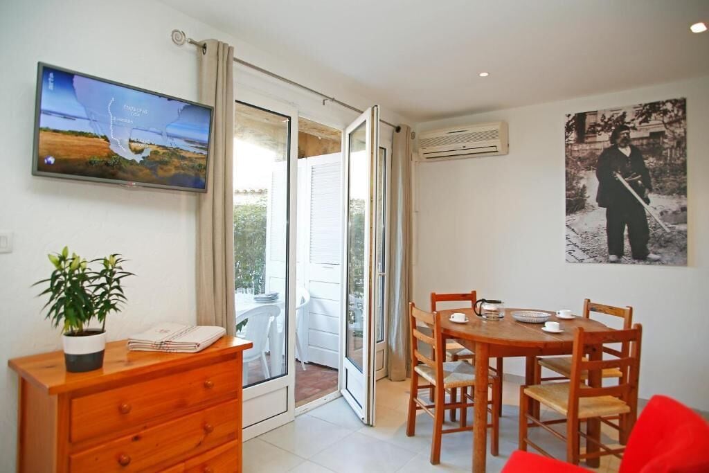 A modern room with a sliding glass door leading to a balcony, a wooden dining table with chairs, a TV mounted on the wall, and a potted plant on a wooden dresser.