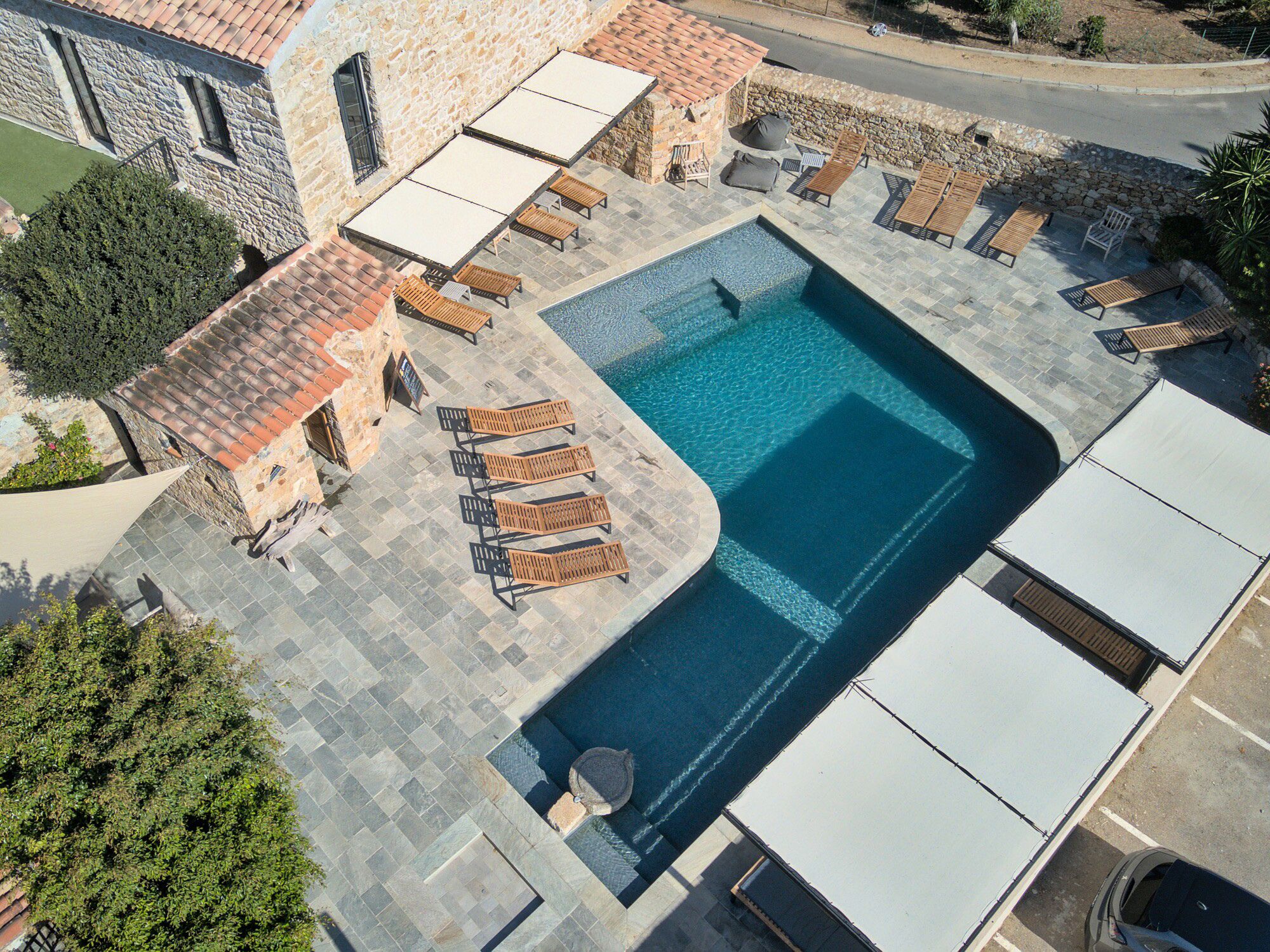 Un área de piscina en la azotea con sillones de descanso y un edificio de piedra.