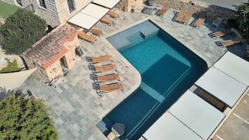 Un área de piscina en la azotea con sillones de descanso y un edificio de piedra.