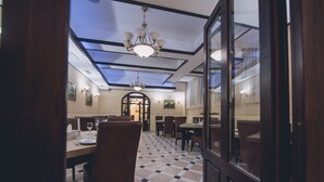 Ein Restaurant mit Schachbrettboden, Holztischen und -stühlen. Eine Glastür befindet sich rechts, und eine Kristallleuchter hängt von der Decke.
