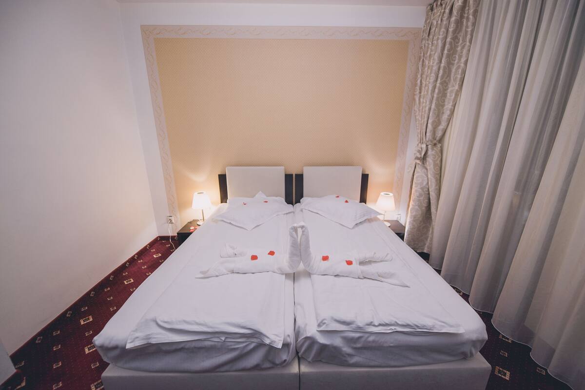 A double bed with white linens and heart-shaped decorations, two bedside lamps, and a red patterned carpet.