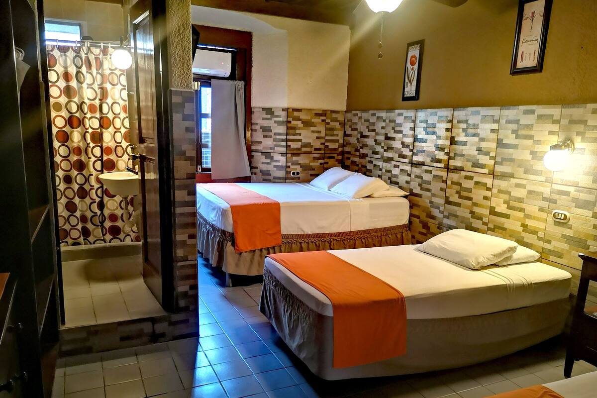 Quarto de hotel com duas camas, banheiro com cortina de chuveiro e parede revestida com azulejos.