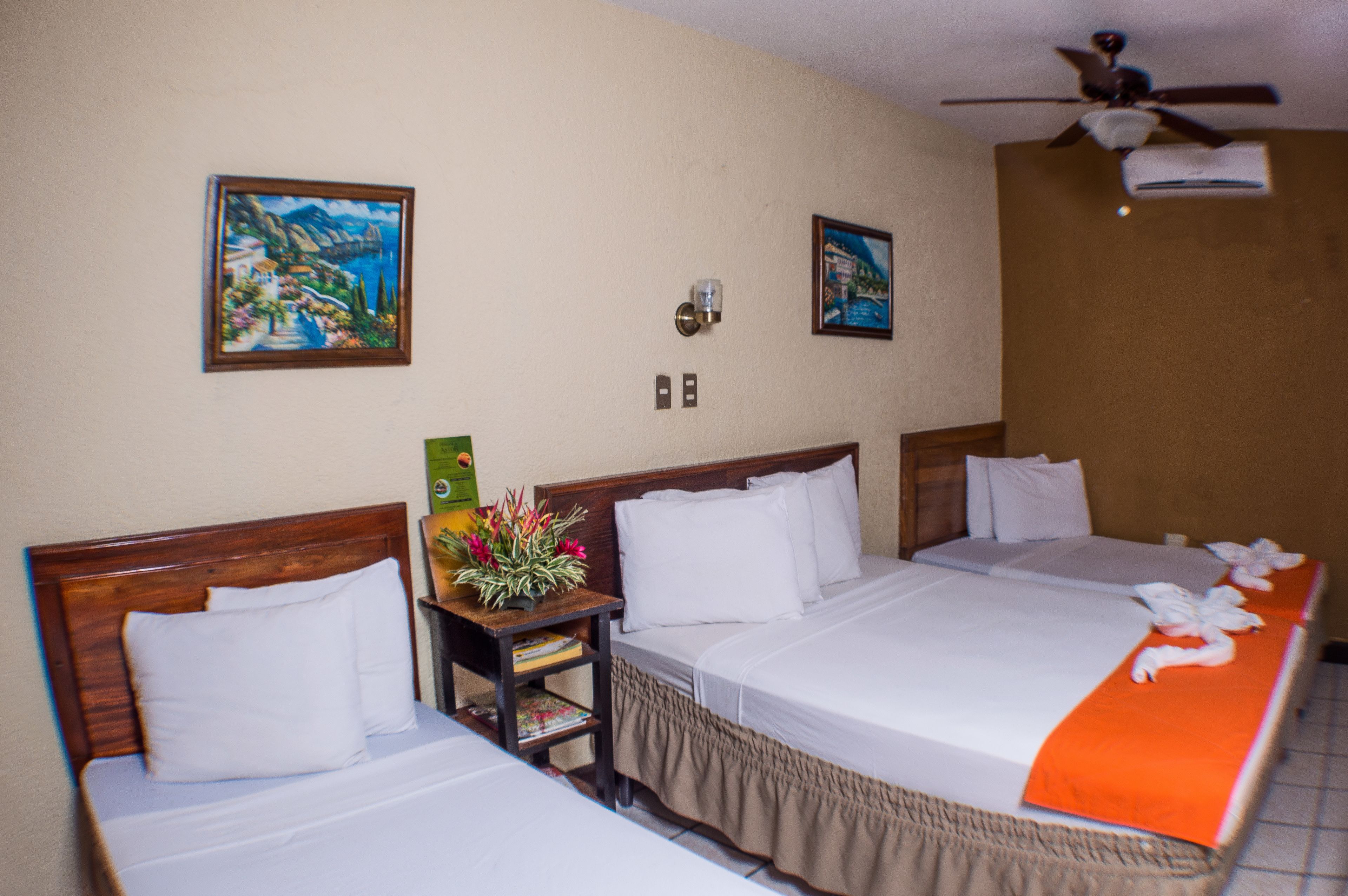 A hotel room with two beds, a ceiling fan, and artwork on the walls.