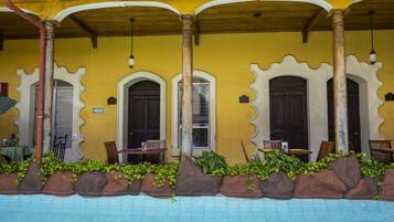 A poolside area with a yellow wall, wooden columns, and a seating area with chairs and tables.