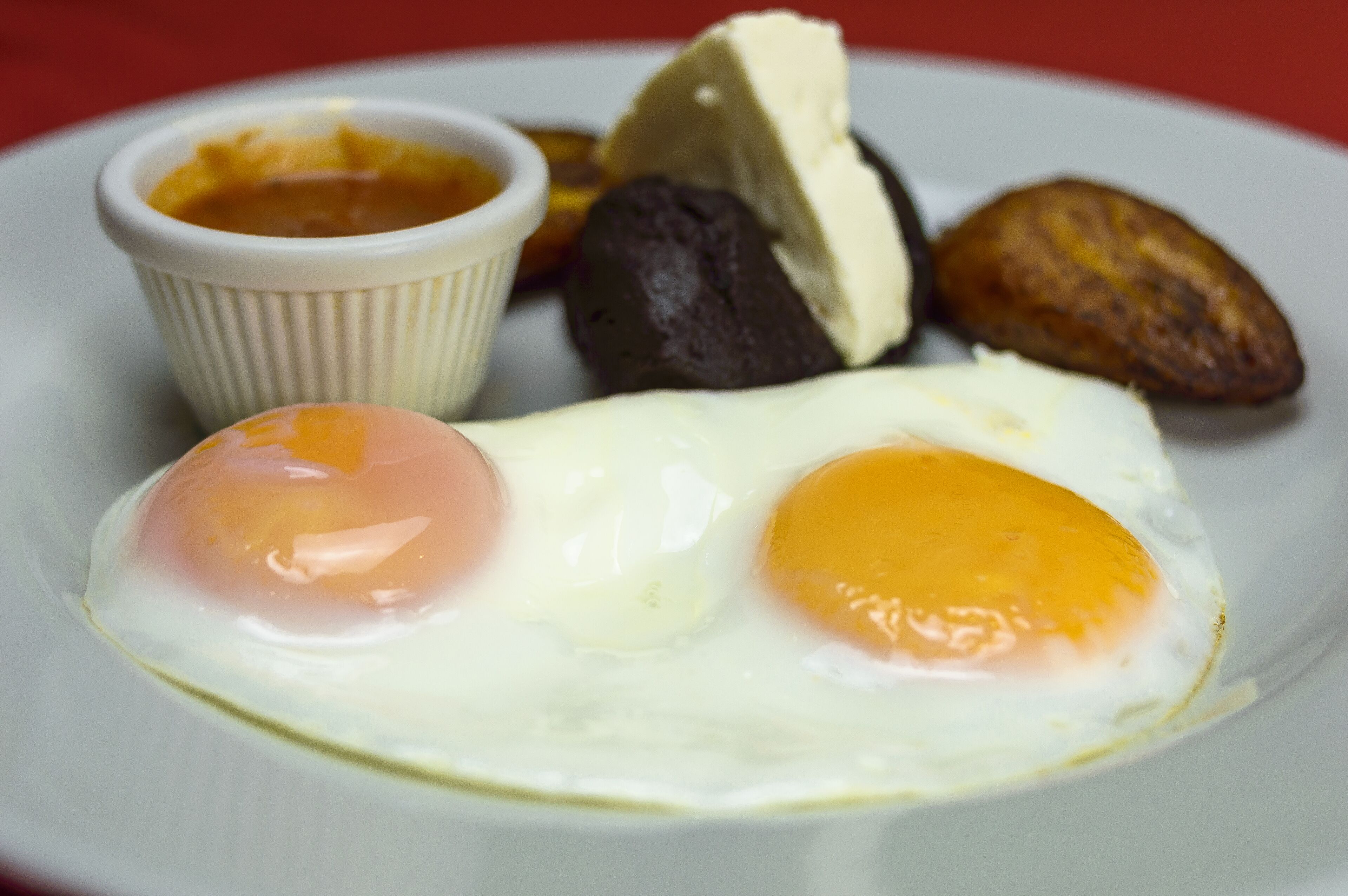 Un plato con dos huevos estrellados, un recipiente pequeño con salsa y varios trozos de carne.