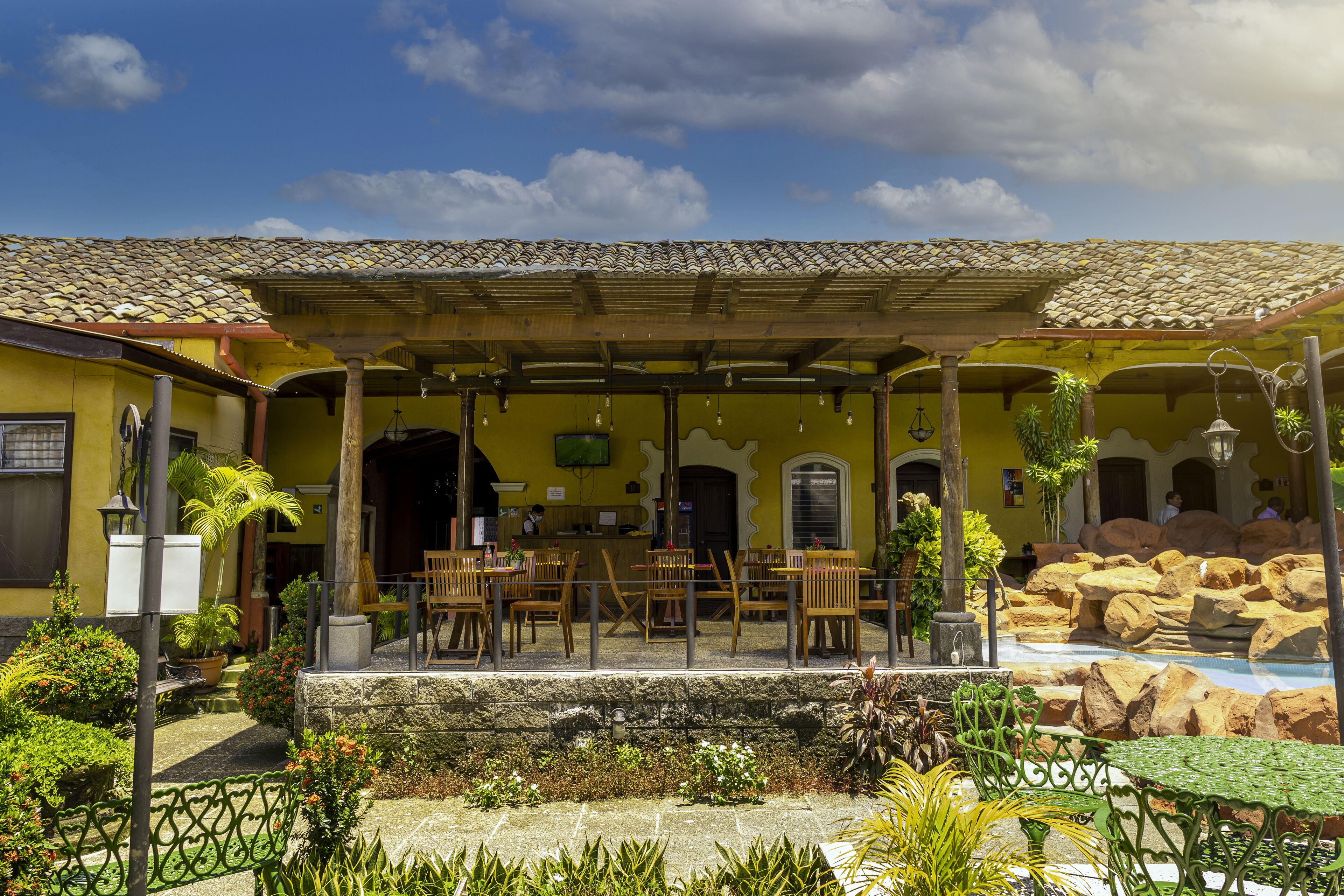 A courtyard with outdoor seating, a pool, and a yellow building with a tiled roof.