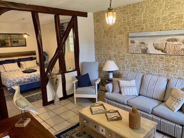 A cozy living room with a stone wall, a sofa, a chair, and a bed with striped bedding.