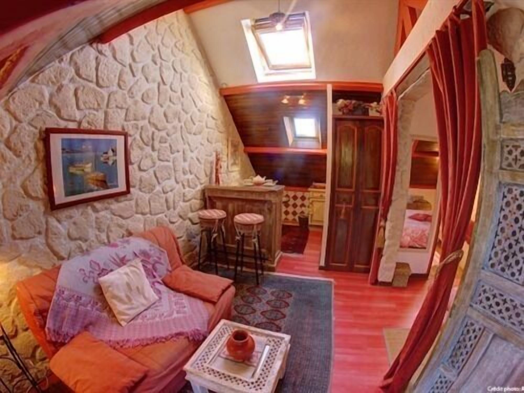 A cozy room with a stone wall, a sofa, a small table with a vase, and a view of a kitchen area.