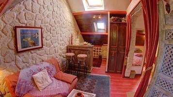 A cozy room with a stone wall, a sofa, a small table with a vase, and a view of a kitchen area.