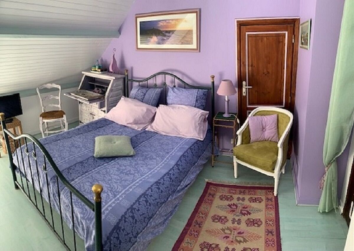 A bedroom with a bed, a chair, a desk, a lamp, and a door.