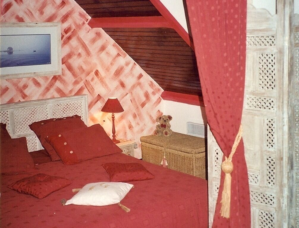 A bedroom with a bed, pillows, a lamp, a teddy bear, and a wicker chest.