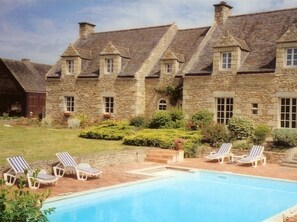 A stone building with a swimming pool and lounge chairs.