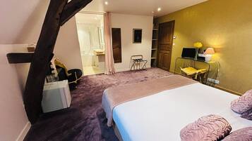 Un dormitorio con cama, escritorio, silla, tocador y un baño visible a través de una puerta abierta.