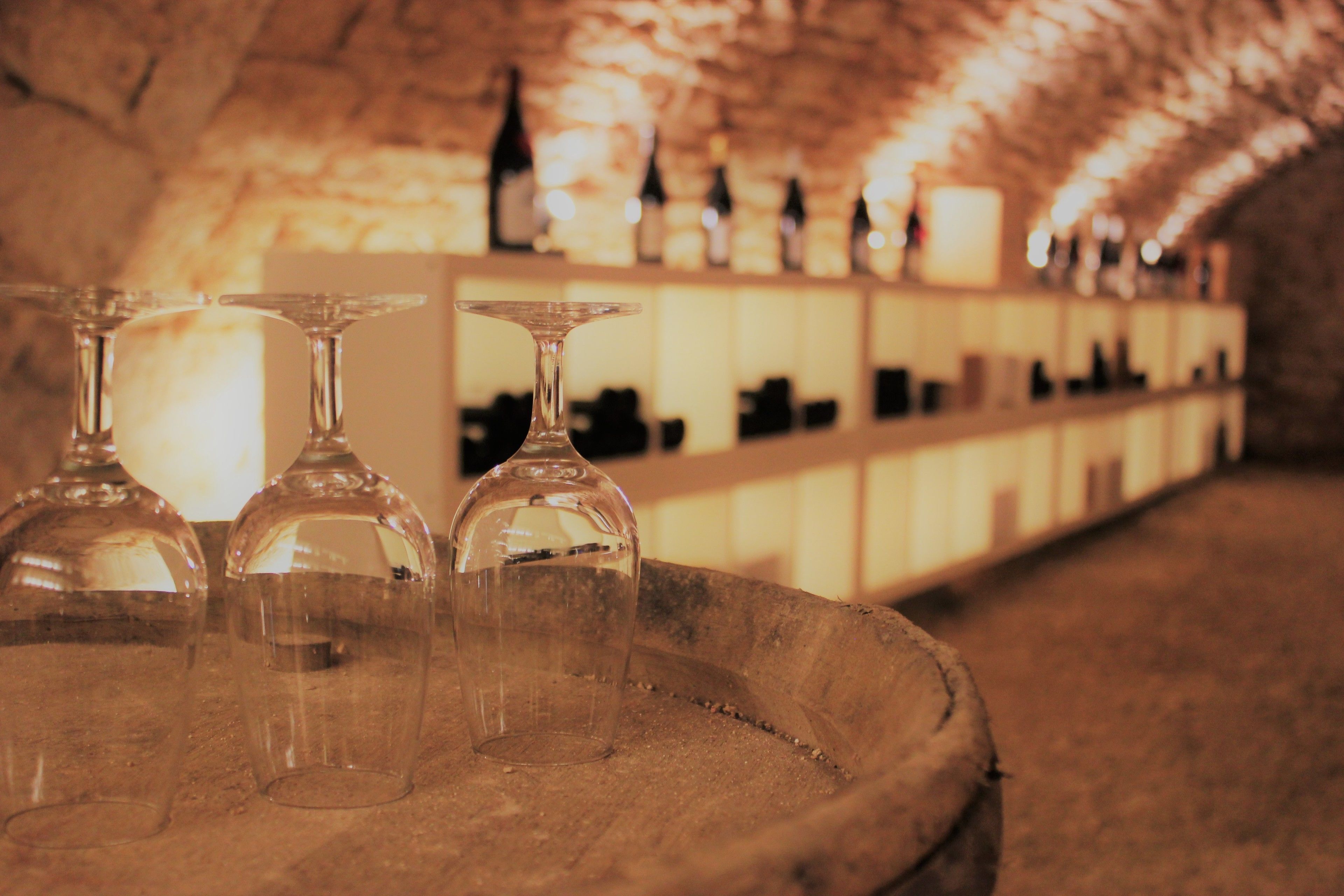 A barrel with three empty wine glasses and a shelf with bottles in the background.