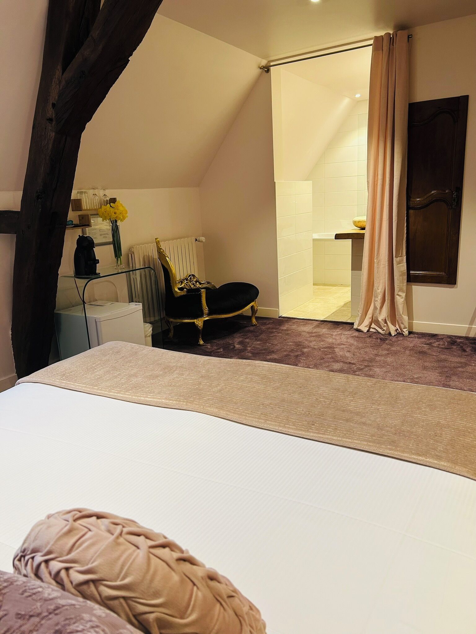 A bedroom with a bed, a chair, a radiator, a mirror, and a bathroom visible through a door.