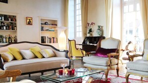 Een goed verlichte woonkamer met een bank, twee fauteuils, een glazen salontafel en een boekenkast.