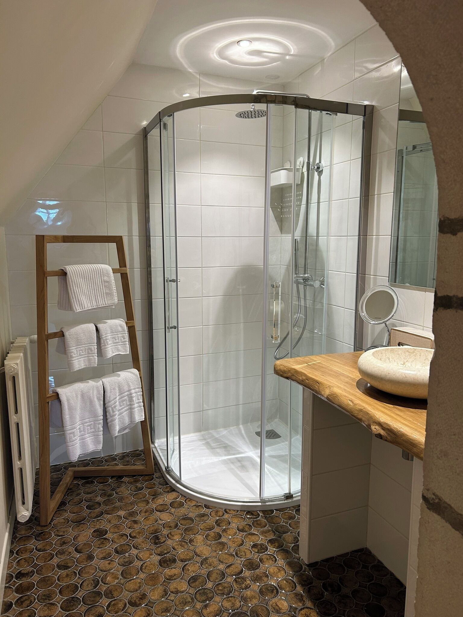 Un baño con cabina de ducha de vidrio, un perchero de madera, un lavabo con encimera de madera y piso de baldosas.