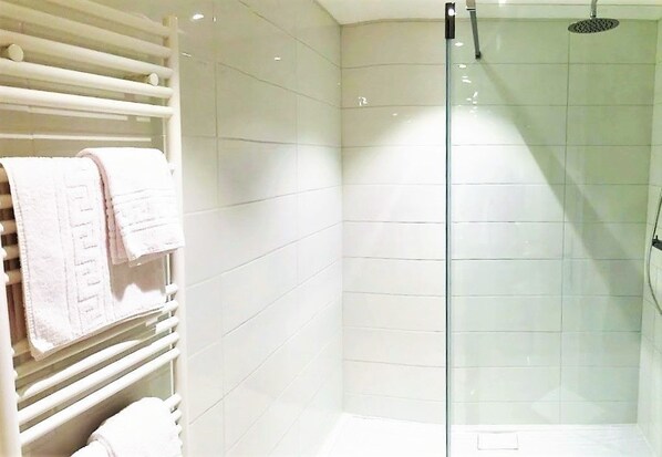 A modern bathroom with white tiled walls, a glass shower enclosure, and a towel rack with neatly folded towels. - Domaine Pont Juillet (Fontaines)