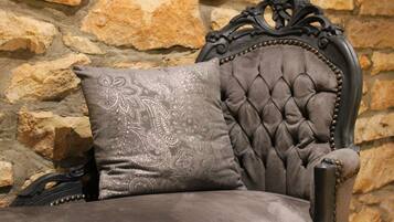 Un fauteuil capitonné avec un coussin décoratif adossé à un mur en pierre.