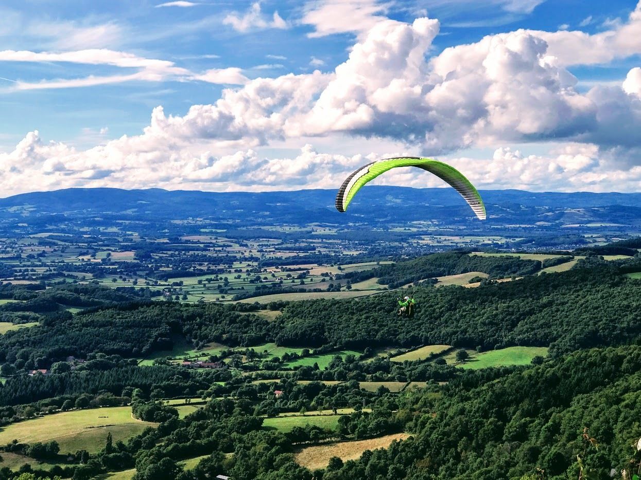 A person paragliding over a landscape with rolling hills and a distant town.
