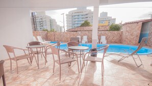 A rooftop pool area with lounge chairs and a table, surrounded by a tiled floor and a view of high-rise buildings. - Hotel Penha (Penha)