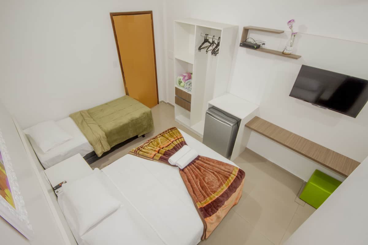 Une chambre d’hôtel de taille réduite, comprenant un lit, un bureau, une télévision et une armoire.