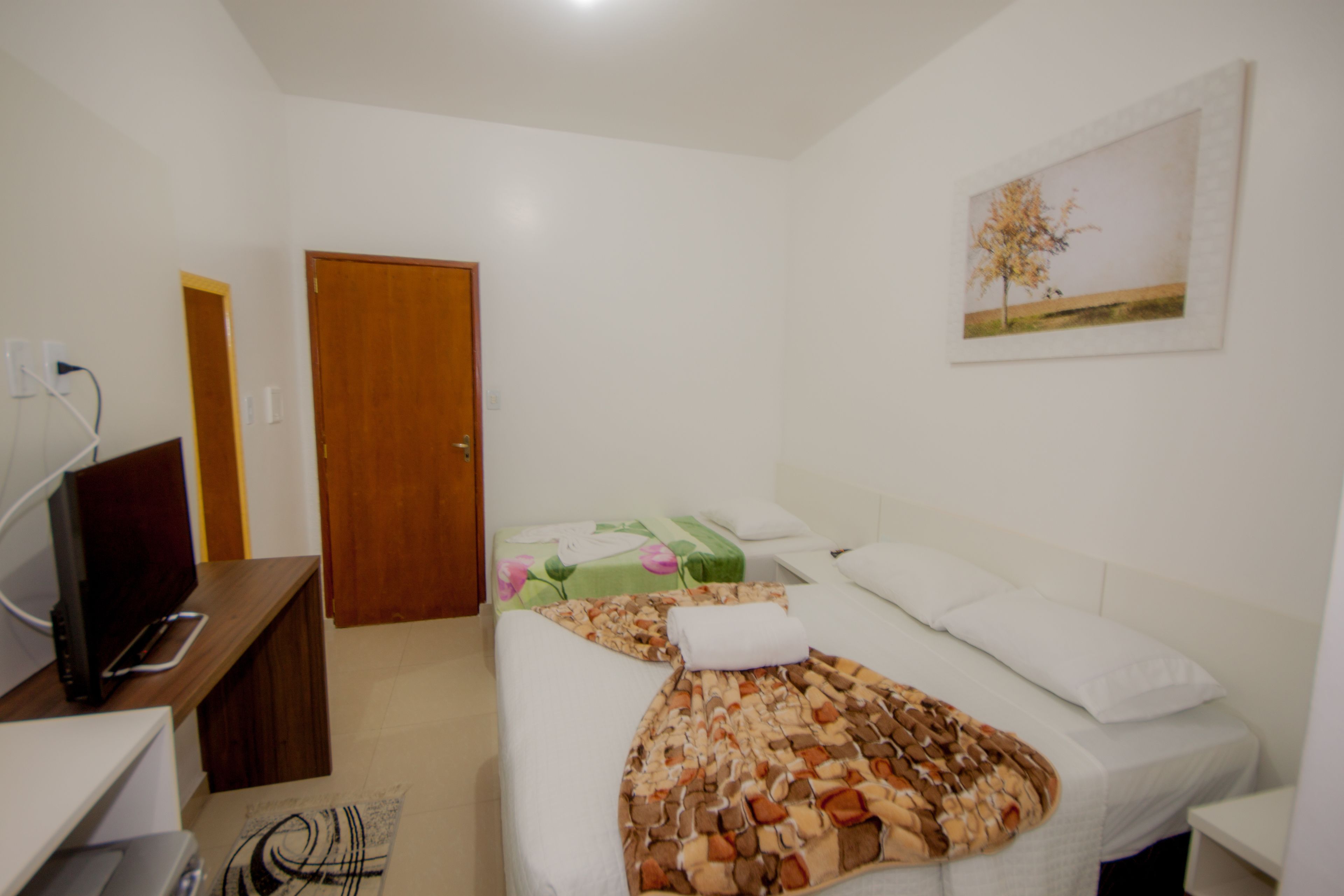 Una habitación de hotel con una cama, un escritorio con computadora, un televisor y un cuadro en la pared.