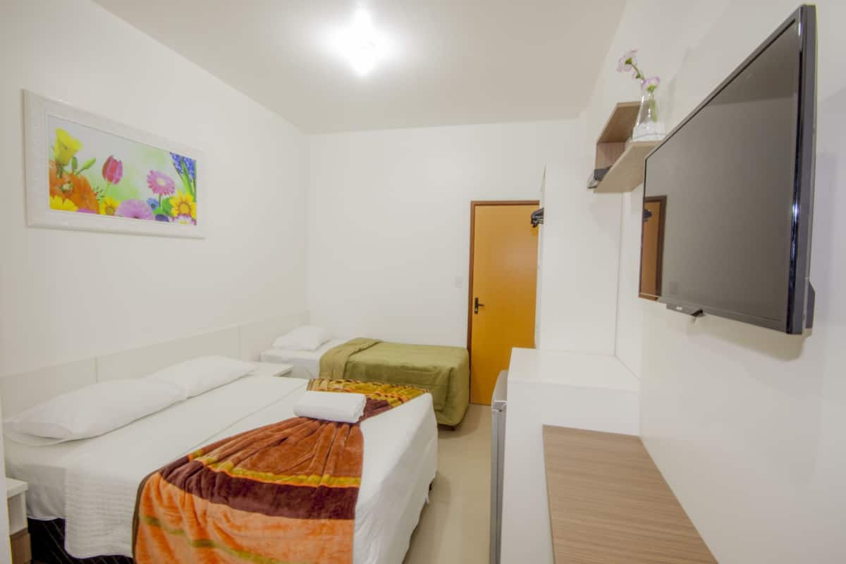 Une chambre d’hôtel avec deux lits simples, un bureau en bois, une télévision et un tableau au mur.