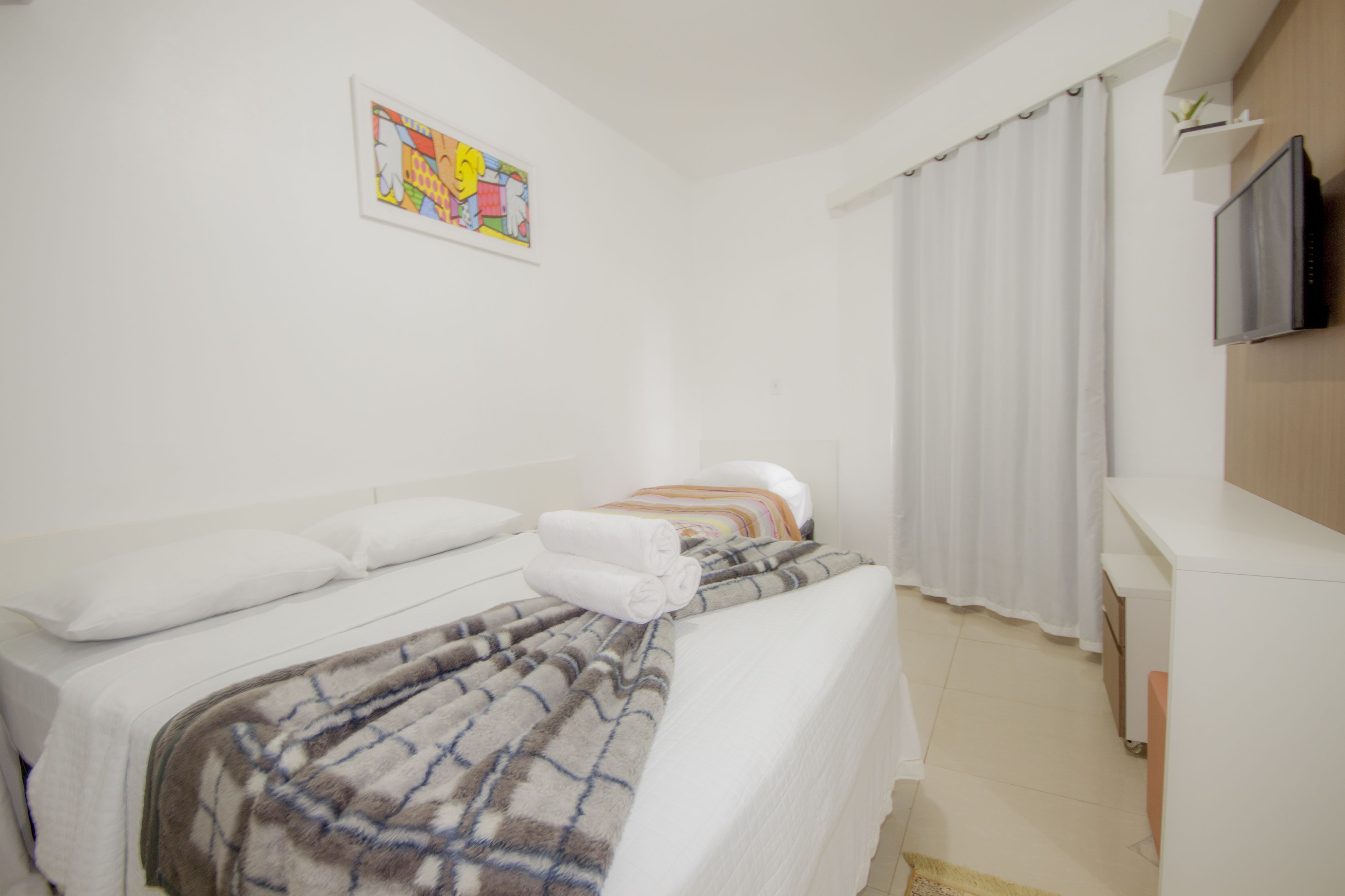 Habitación de hotel con cama, televisión, un cuadro en la pared y ventana con cortinas.