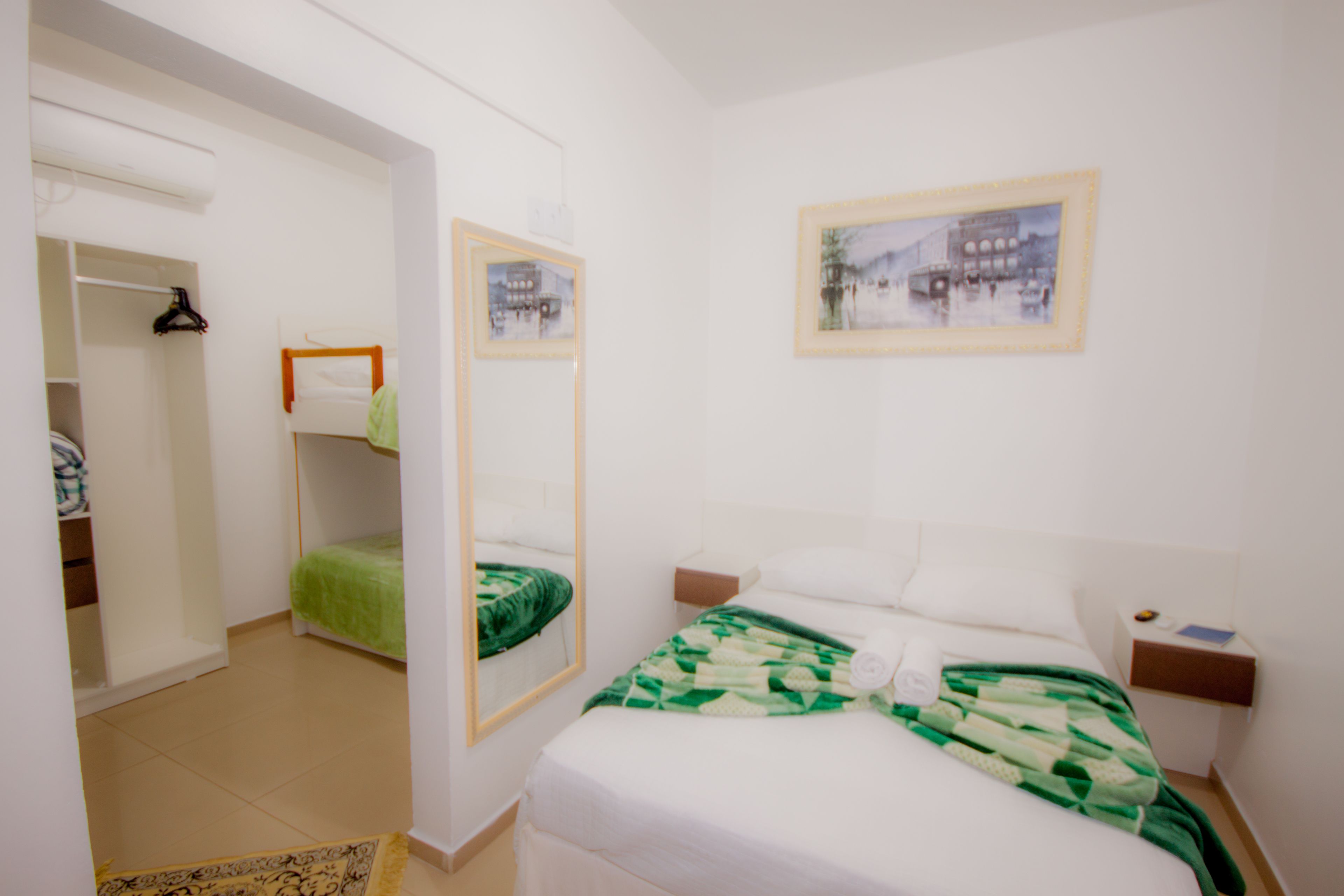 A hotel room with a bed, a bedside table, a nightstand, a mirror, a wardrobe, and a framed picture on the wall.