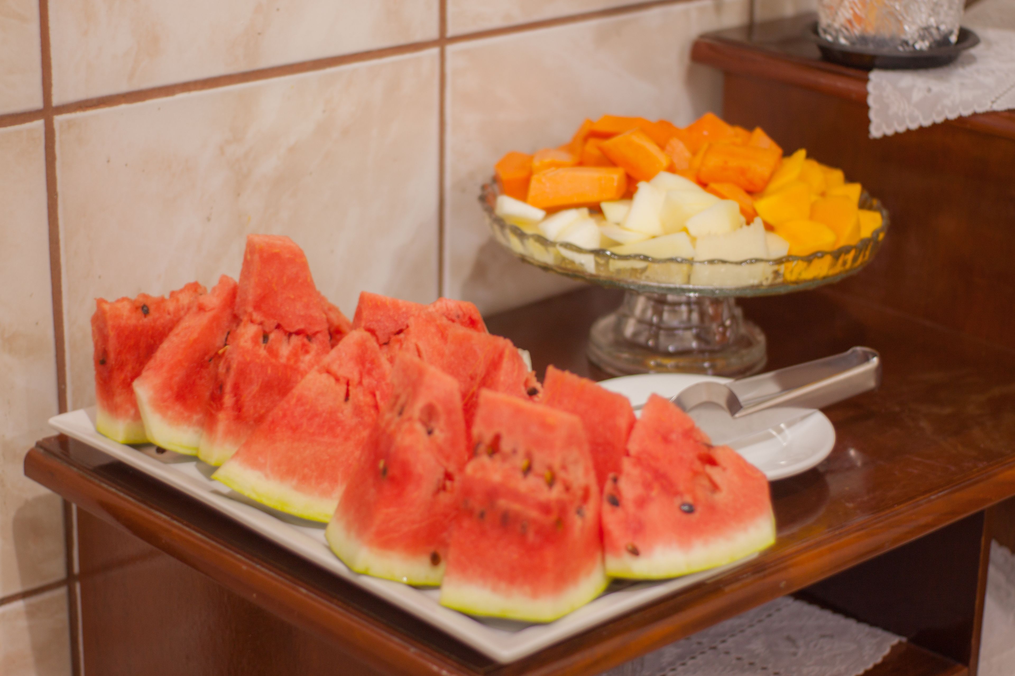 A plate of watermelon slices and a bowl of assorted fruit on a wooden table.