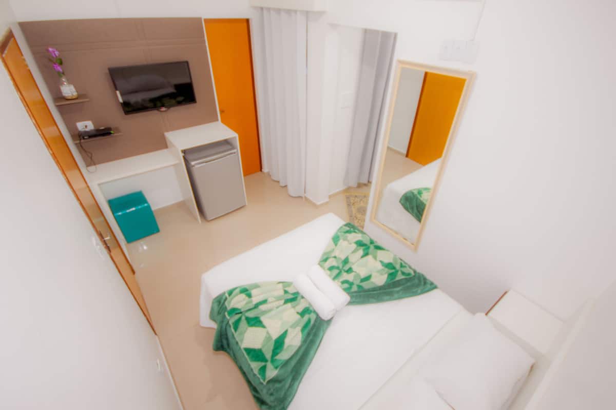 Une chambre d’hôtel avec un lit, un bureau, une télévision et un miroir.