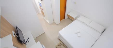 Un dormitorio con cama, escritorio con computadora, armario y puerta que da a otra habitación.