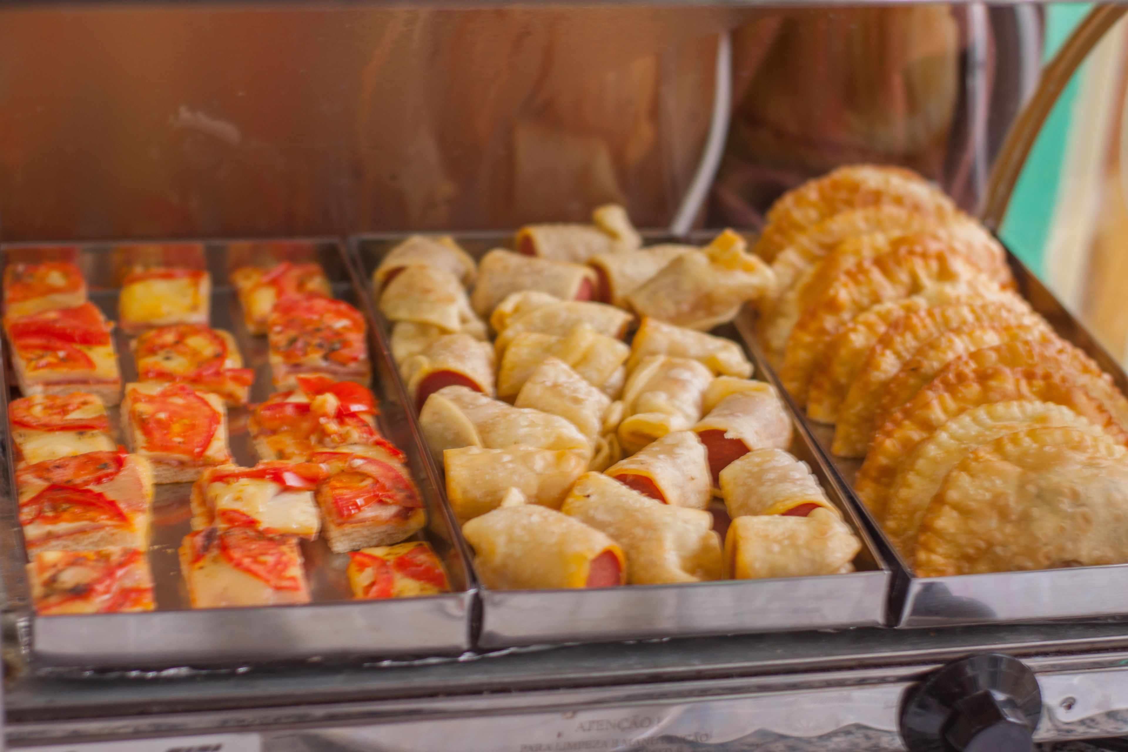 Exposição de comida com diversos itens, incluindo fatias de pizza e doces.