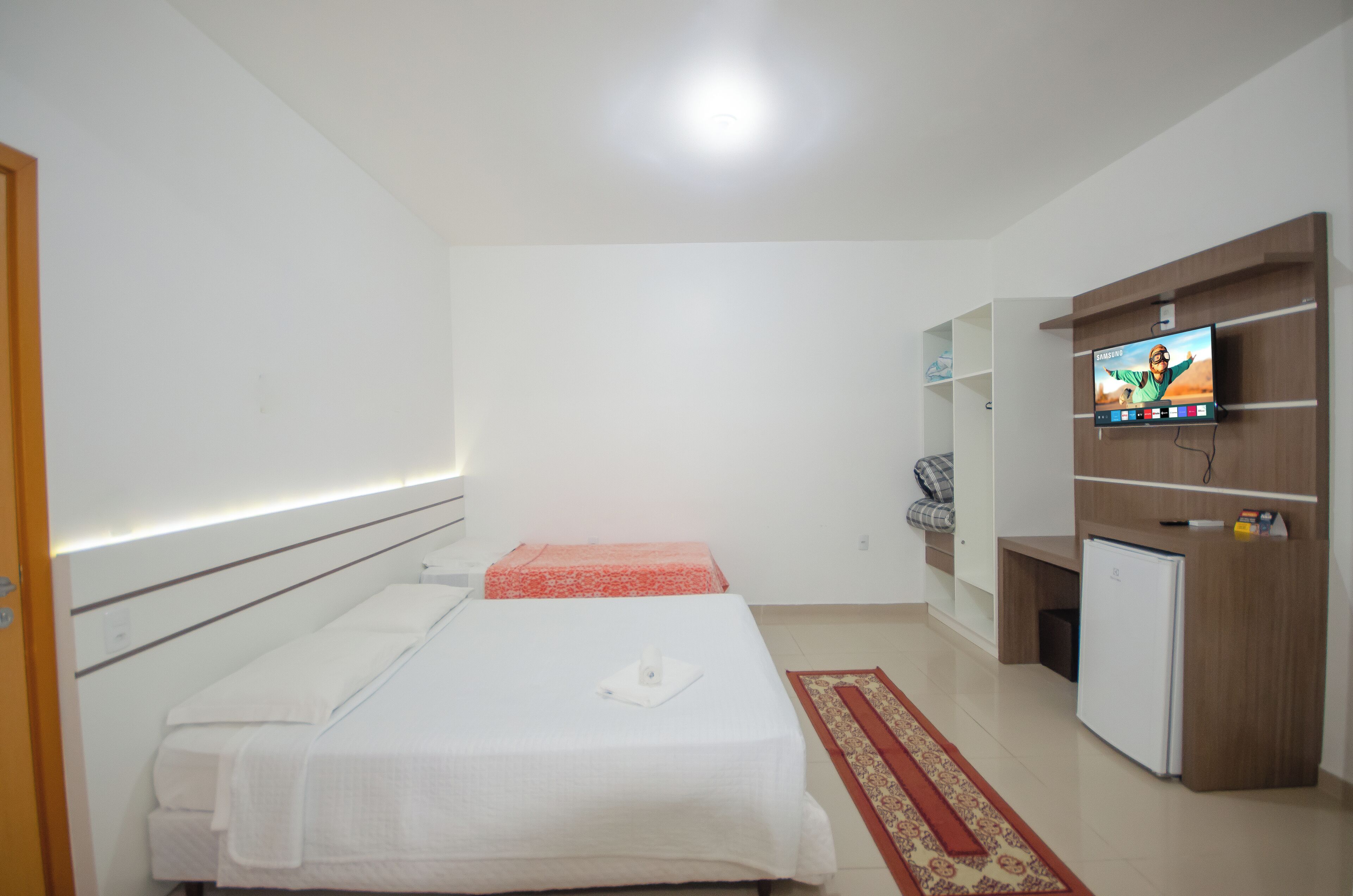 Habitación de hotel con dos camas, televisión, mini refrigerador y un mueble de madera.