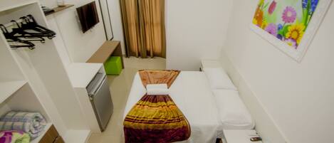 A compact hotel room with a bed, a small desk, a wardrobe, and a shower area.