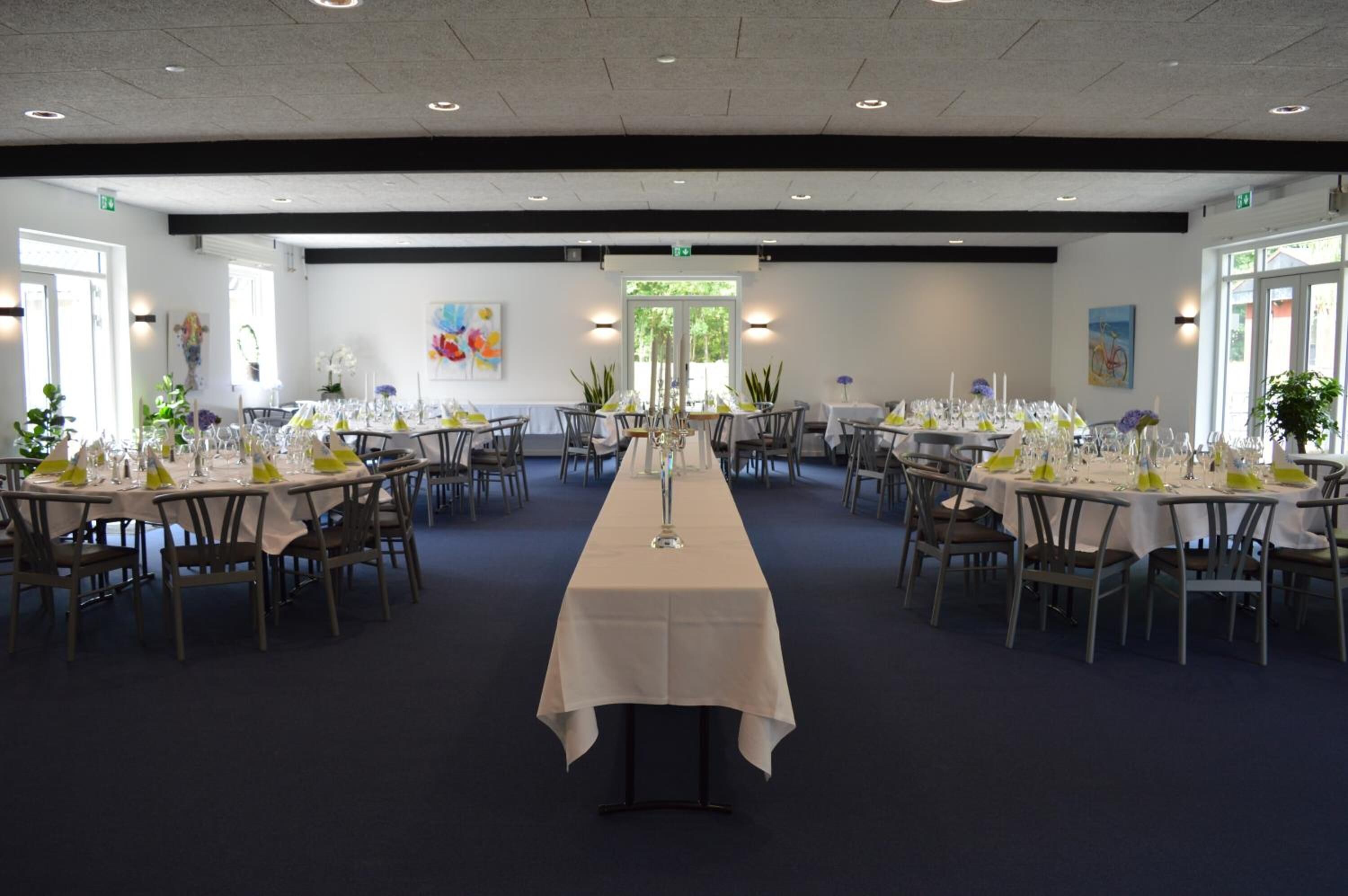 A large banquet hall with long tables set for dining, featuring white tablecloths and green centerpieces.