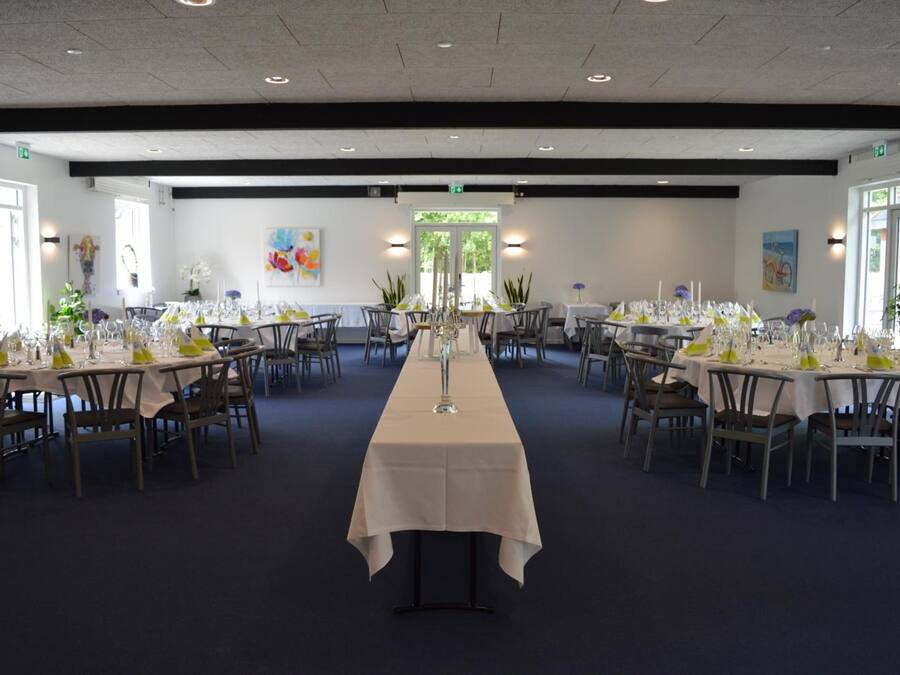 A large banquet hall with long tables set for dining, featuring white tablecloths and green centerpieces.
