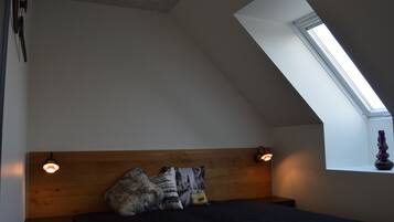 Un dormitorio con techo inclinado, tragaluces, cama con cabecera de madera y dos lámparas de noche.